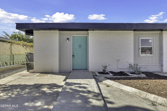 entrance to property featuring fence and brick siding