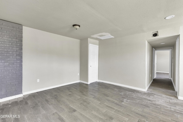 unfurnished room with a textured ceiling, wood finished floors, and baseboards