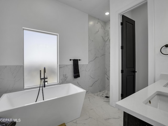 full bathroom with marble finish floor, tile walls, double vanity, recessed lighting, and a freestanding bath