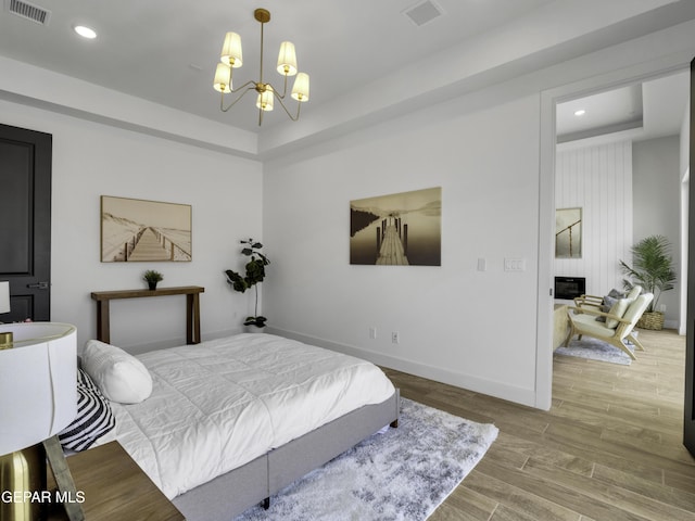 bedroom featuring visible vents, a chandelier, wood finished floors, and a raised ceiling