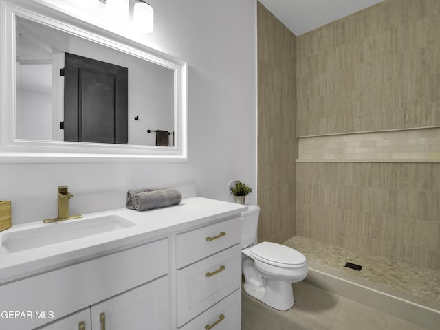 bathroom with toilet, tile patterned flooring, tiled shower, and vanity