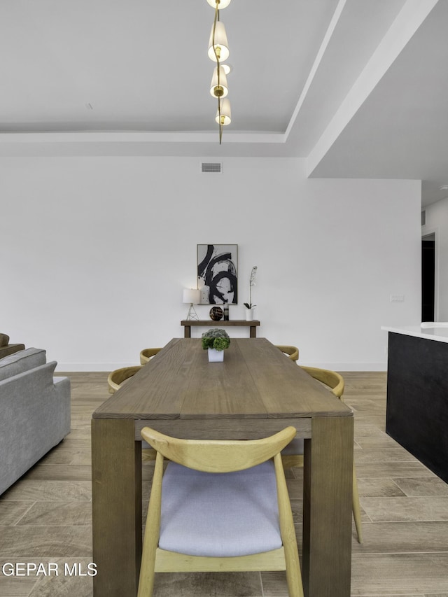 dining area with a raised ceiling, visible vents, baseboards, and wood finished floors