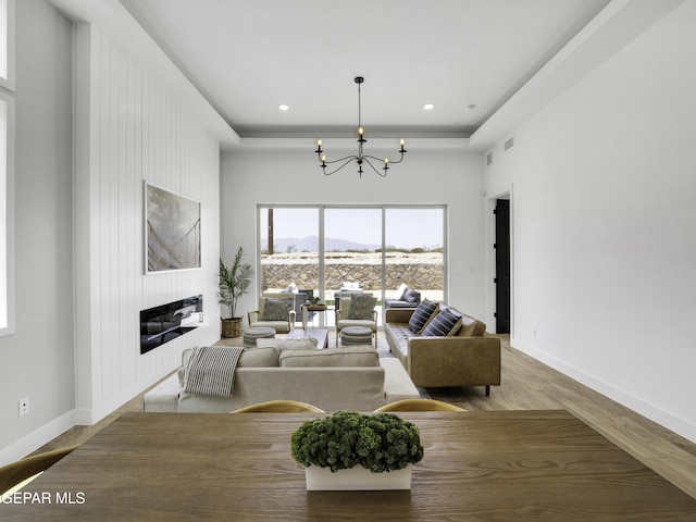 living area with a tray ceiling, a fireplace, an inviting chandelier, a mountain view, and baseboards