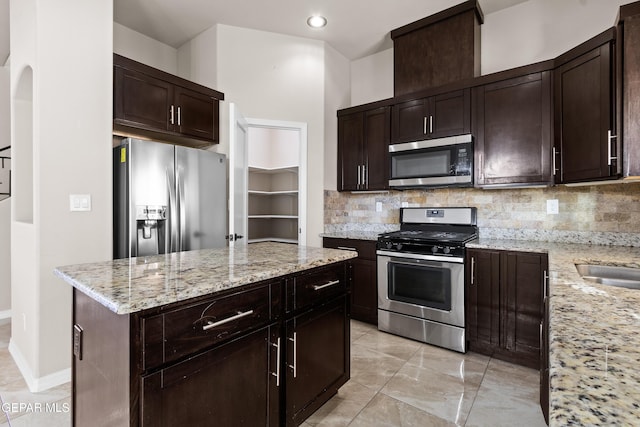 kitchen with dark brown cabinetry, light stone counters, stainless steel appliances, and backsplash