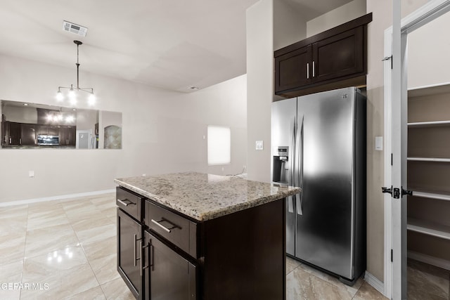 kitchen featuring dark brown cabinetry, stainless steel fridge, visible vents, a center island, and light stone countertops