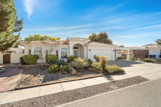 mediterranean / spanish house with a garage, fence, a tiled roof, driveway, and stucco siding