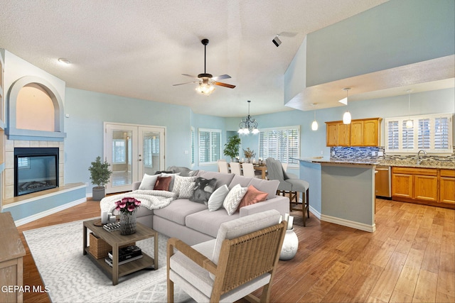 living room featuring a tiled fireplace, baseboards, vaulted ceiling, and light wood finished floors