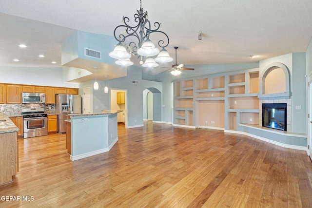 kitchen featuring arched walkways, stainless steel appliances, visible vents, light wood-style flooring, and a tiled fireplace