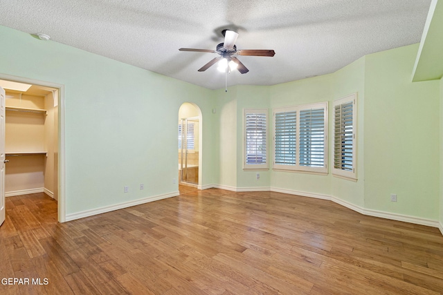 empty room featuring a ceiling fan, a textured ceiling, arched walkways, and wood finished floors