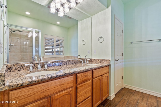 bathroom featuring double vanity, a shower stall, a sink, and wood finished floors