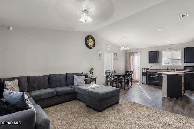 living room with dark wood-type flooring, visible vents, vaulted ceiling, and ceiling fan with notable chandelier