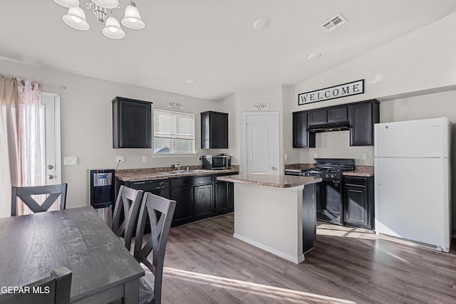 kitchen with black gas range, visible vents, dark cabinetry, freestanding refrigerator, and a center island