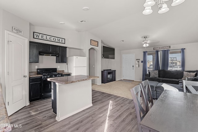 kitchen featuring open floor plan, black gas stove, freestanding refrigerator, and dark cabinets