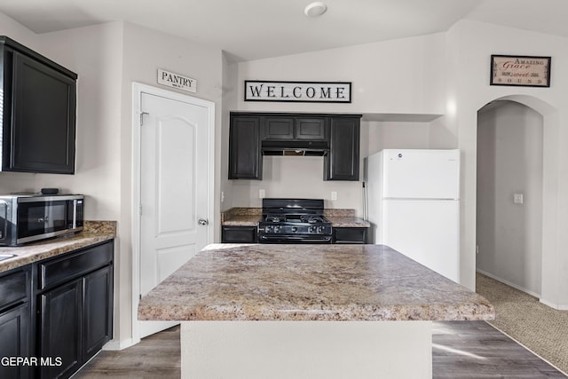 kitchen featuring arched walkways, black gas range oven, lofted ceiling, stainless steel microwave, and freestanding refrigerator