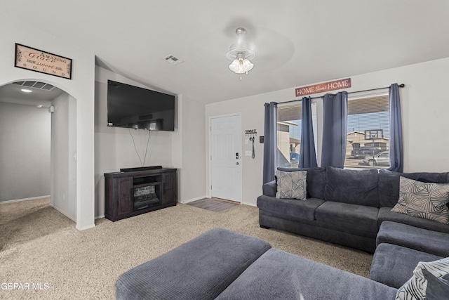 carpeted living room featuring arched walkways, ceiling fan, visible vents, and baseboards