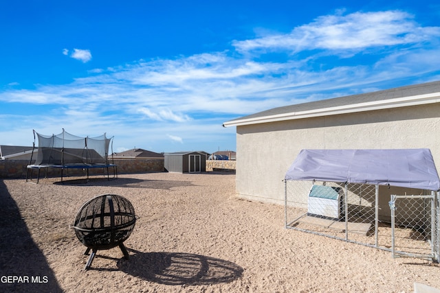 view of yard featuring an outdoor fire pit, a trampoline, a shed, and an outbuilding