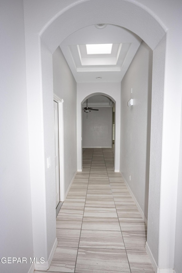 corridor featuring arched walkways, a raised ceiling, and baseboards