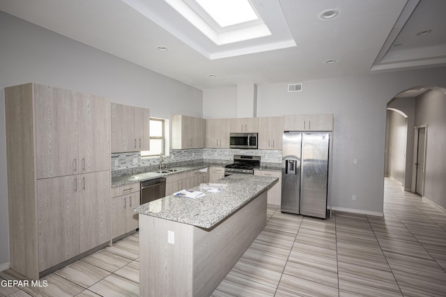 kitchen with arched walkways, decorative backsplash, light stone countertops, stainless steel appliances, and light brown cabinets