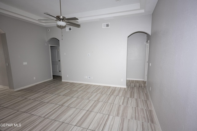 empty room featuring arched walkways, a raised ceiling, visible vents, and baseboards