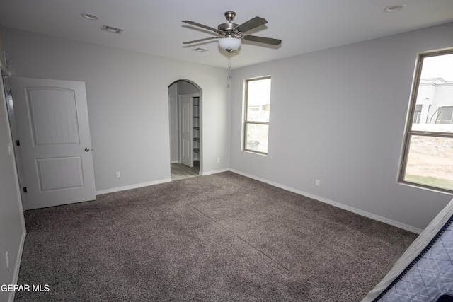 spare room featuring arched walkways, carpet, visible vents, and baseboards