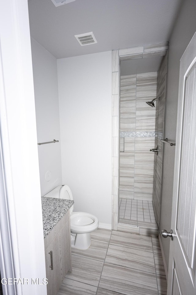 full bath featuring toilet, visible vents, a tile shower, and vanity