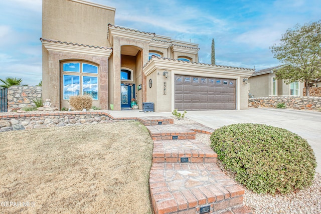 mediterranean / spanish house featuring a garage, driveway, a tiled roof, and stucco siding