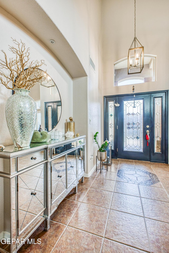 entryway with a chandelier, a high ceiling, visible vents, and baseboards