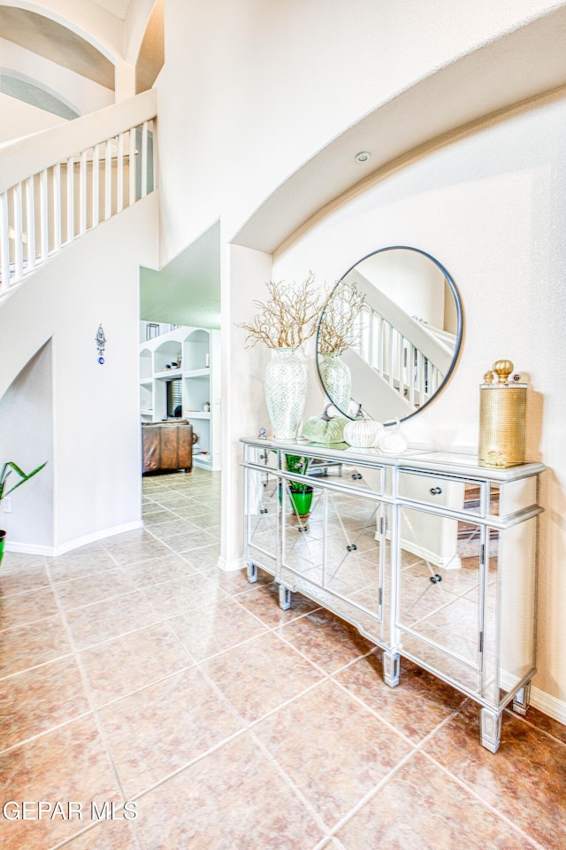 hall with a high ceiling, baseboards, and tile patterned floors