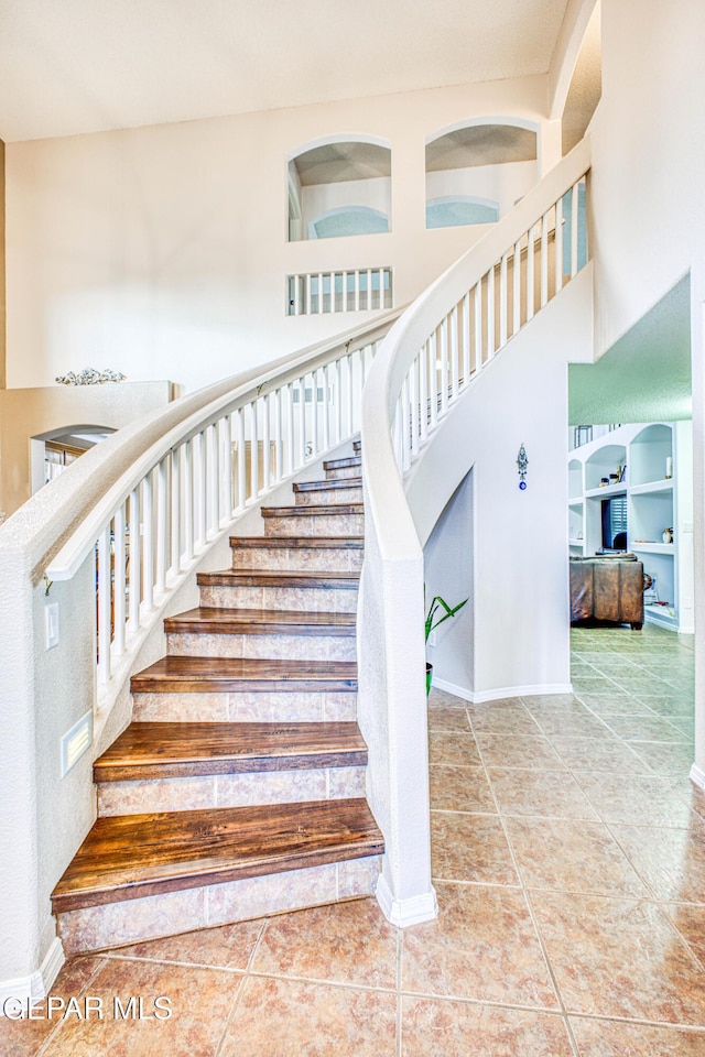 stairs featuring tile patterned flooring, a towering ceiling, and baseboards