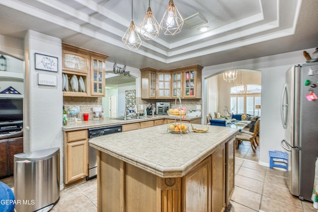 kitchen with stainless steel appliances, a sink, a kitchen island, tasteful backsplash, and a raised ceiling