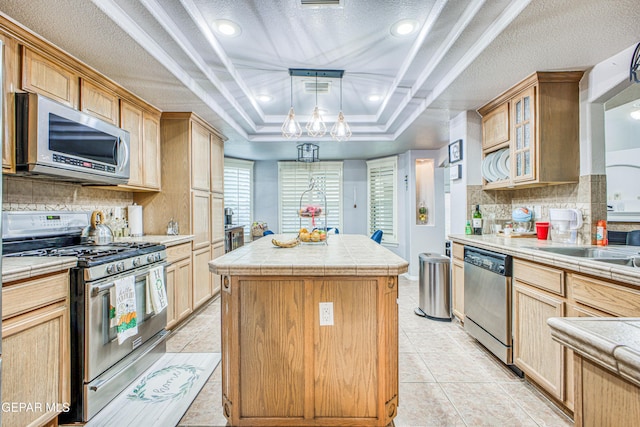 kitchen with a tray ceiling, a center island, tile counters, visible vents, and appliances with stainless steel finishes