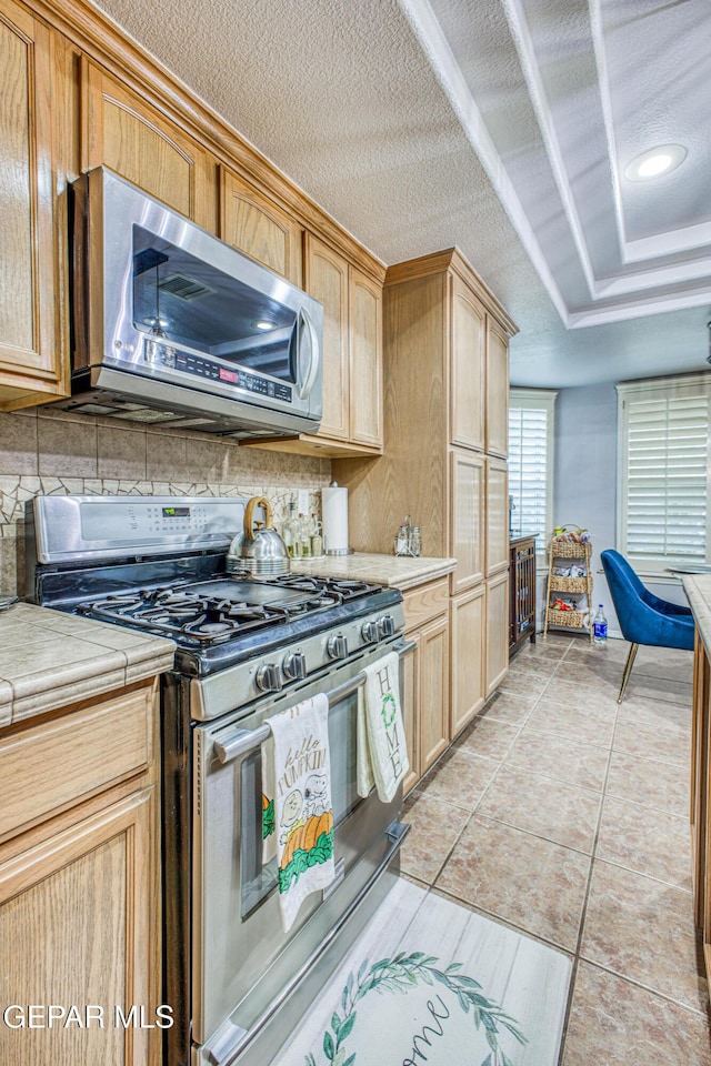 kitchen featuring light tile patterned floors, tasteful backsplash, stainless steel appliances, and light countertops