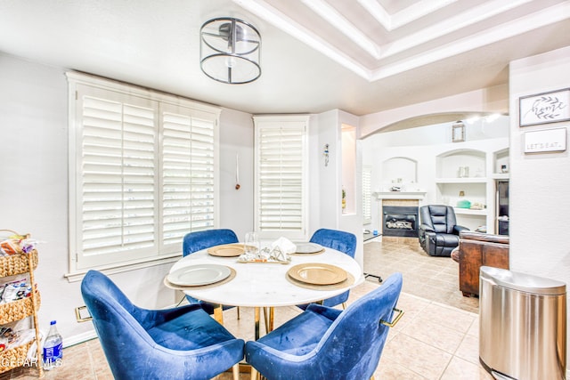 dining space with light tile patterned floors, baseboards, arched walkways, a glass covered fireplace, and built in shelves