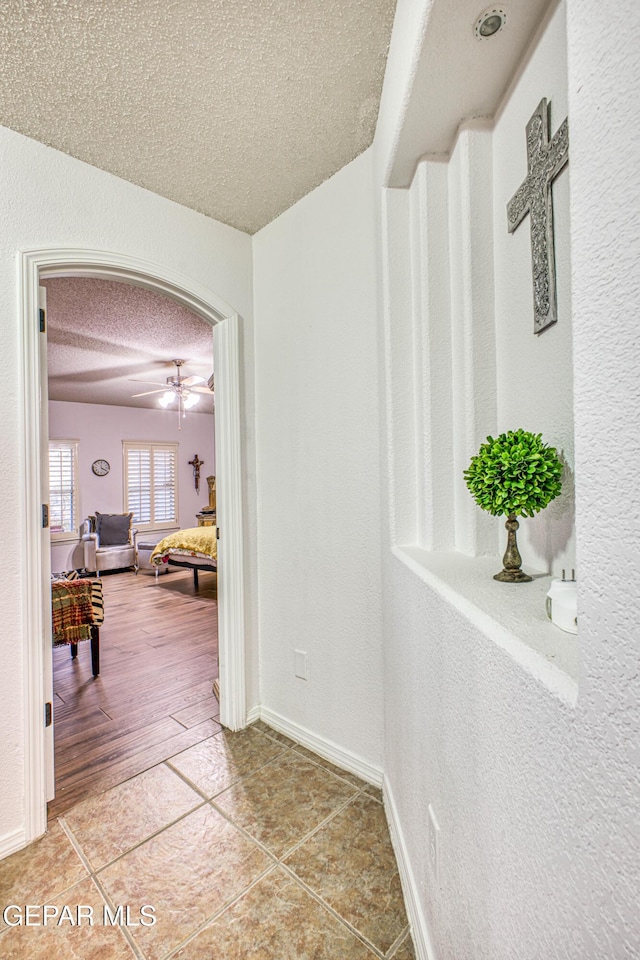 hall with light tile patterned floors, baseboards, arched walkways, a textured wall, and a textured ceiling