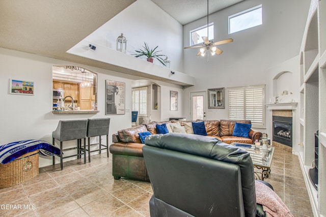 tiled living area with ceiling fan, a textured ceiling, a glass covered fireplace, and a wealth of natural light