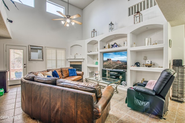 living room featuring built in features, a fireplace, a high ceiling, a ceiling fan, and tile patterned floors