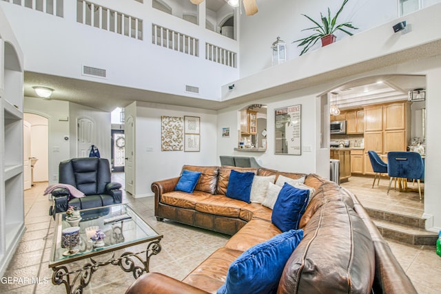 living room with arched walkways, light tile patterned floors, visible vents, and a ceiling fan