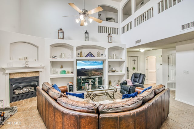 living room featuring built in shelves, visible vents, a tiled fireplace, a ceiling fan, and tile patterned flooring