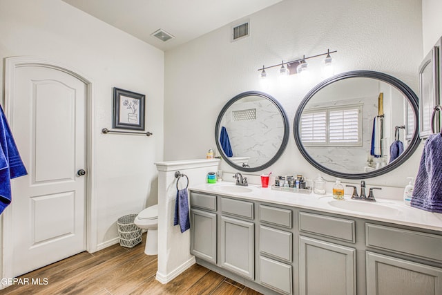 bathroom with double vanity, visible vents, a sink, and wood finished floors