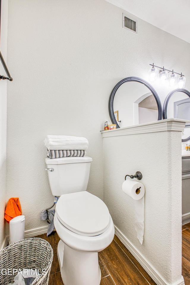 bathroom with toilet, visible vents, baseboards, and wood finished floors