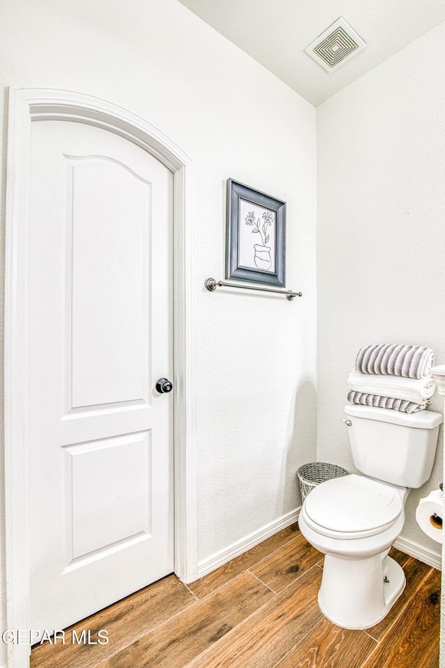 bathroom featuring toilet, wood finished floors, visible vents, and baseboards