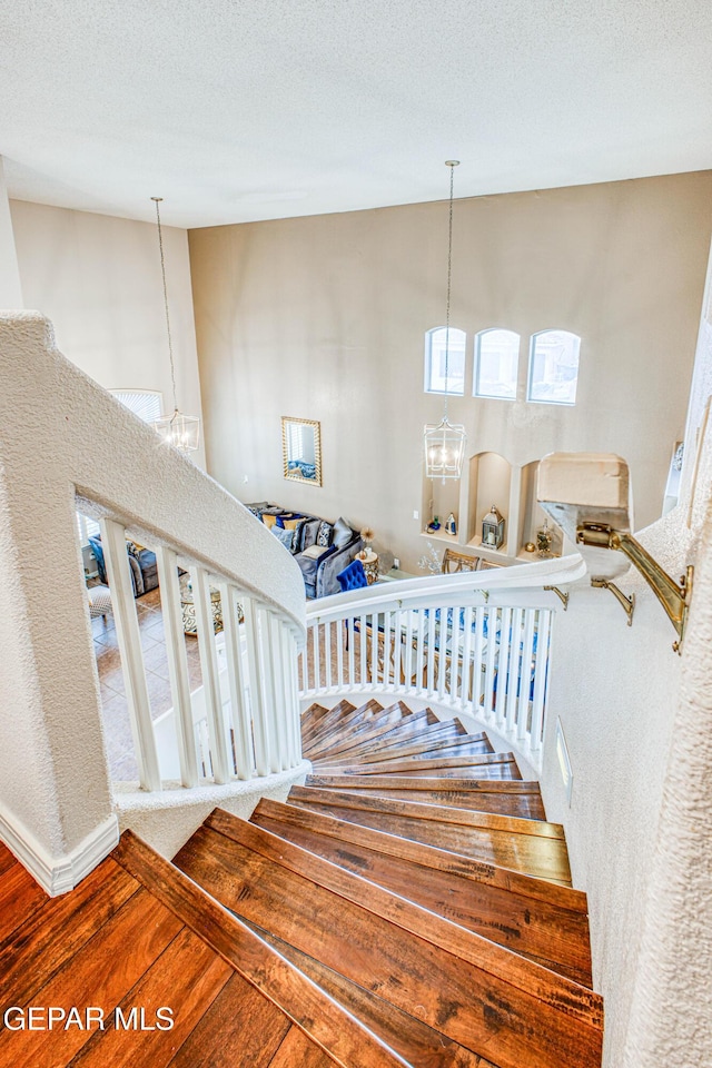 staircase featuring a textured ceiling, wood finished floors, and an inviting chandelier