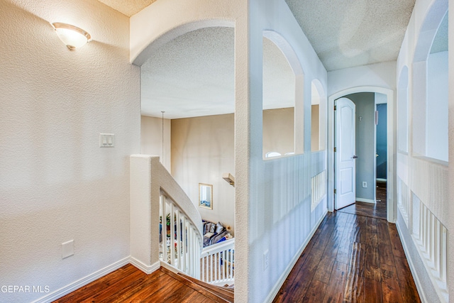 hall featuring a textured ceiling, a textured wall, hardwood / wood-style floors, and baseboards