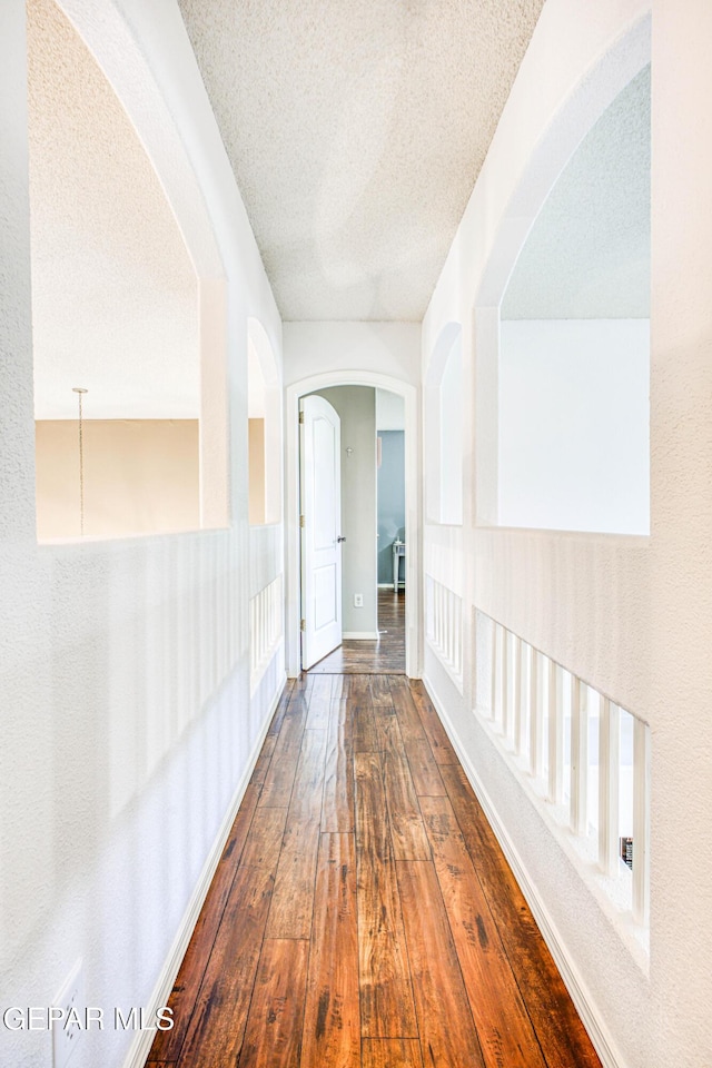 corridor with a textured ceiling, hardwood / wood-style flooring, and baseboards