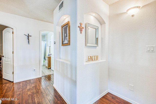 hallway with baseboards, visible vents, arched walkways, and dark wood-style flooring