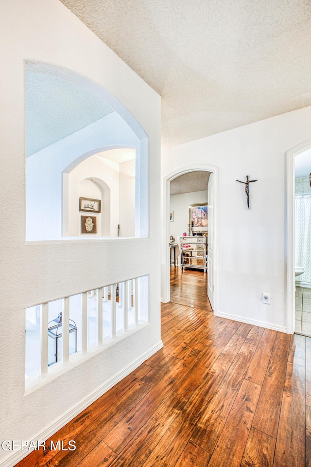 corridor with a textured ceiling, baseboards, and hardwood / wood-style flooring