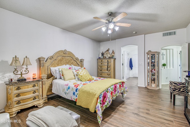 bedroom with arched walkways, visible vents, a textured ceiling, and wood finished floors