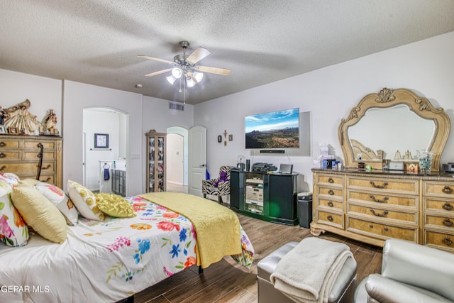 bedroom featuring visible vents, arched walkways, a ceiling fan, wood finished floors, and a textured ceiling