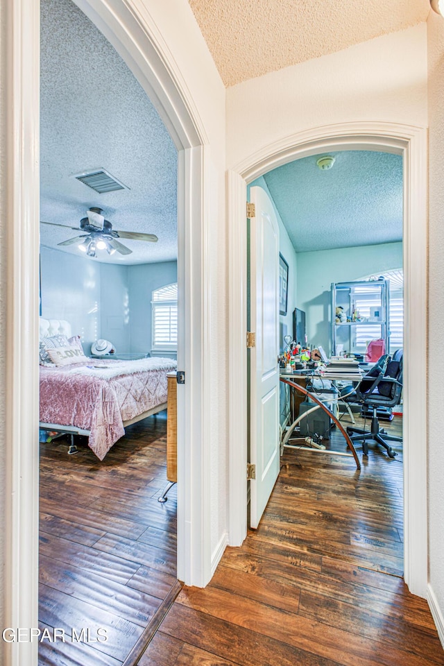 hallway featuring visible vents, a textured ceiling, arched walkways, and hardwood / wood-style floors