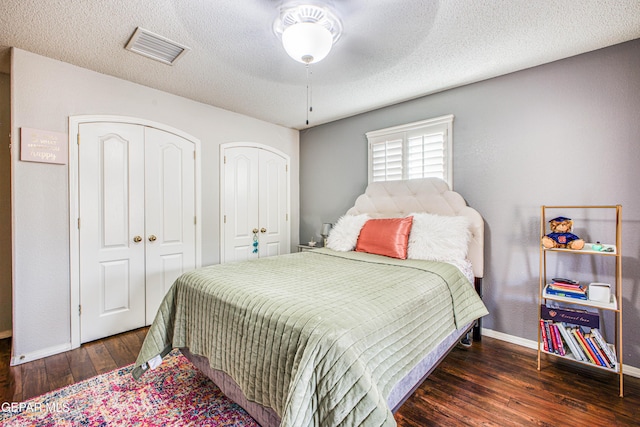 bedroom featuring two closets, visible vents, a textured ceiling, wood finished floors, and baseboards